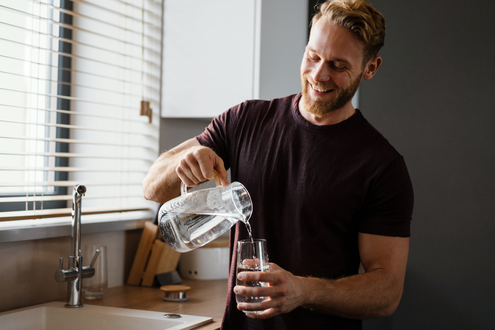 Attraktiver junger Mann gießt Wasser aus einem Krug in ein Glas