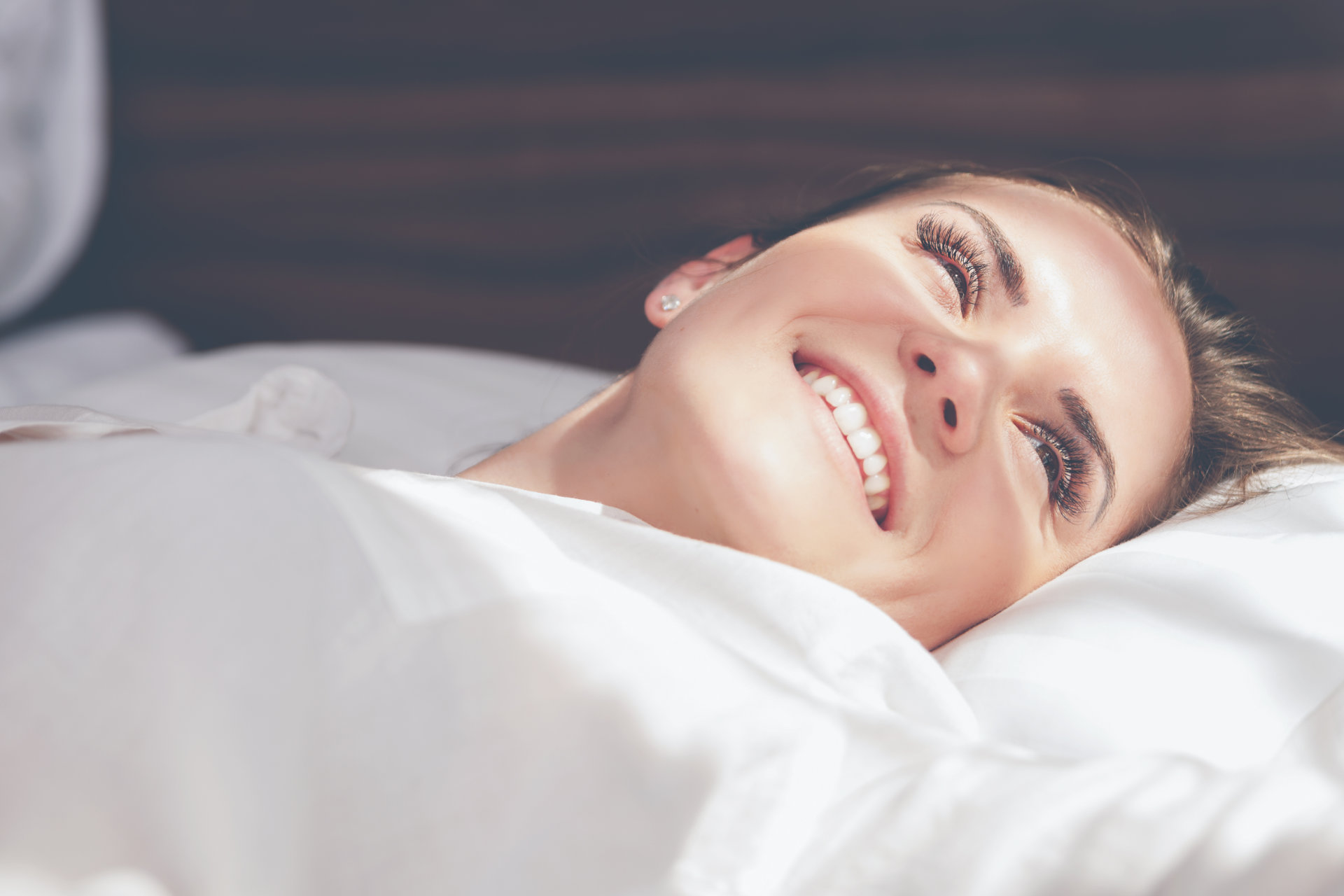 Hübsche Frau auf dem Bett in moderner Wohnung lächelt nach dem Aufwachen